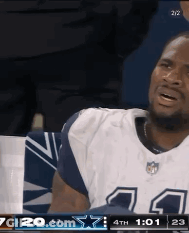 A Man In A Cowboys Jersey Is Sitting In The Stands During A Game . GIF