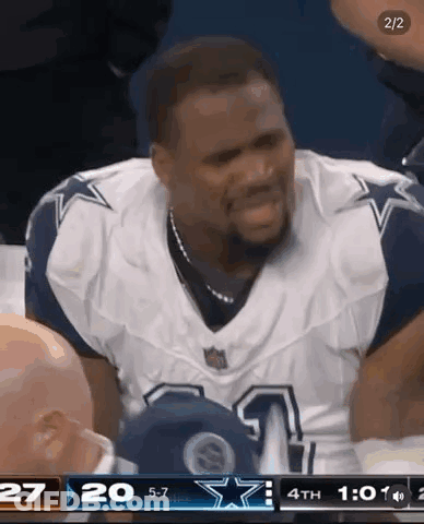 A Man In A Cowboys Uniform Is Sitting In The Stands During A Football Game . GIF