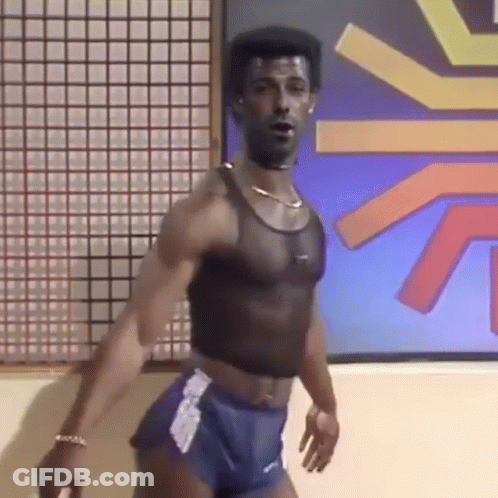 A Man In A Crop Top And Shorts Is Standing In Front Of A Wall . GIF