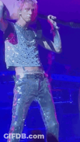 A Man In A Crop Top Is Holding A Guitar And Singing Into A Microphone . GIF