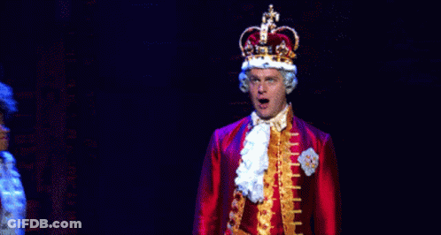 A Man In A Crown Stands Next To A Woman In A Red Coat . GIF