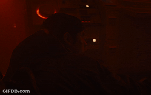 A Man In A Dark Room With A Red Background GIF