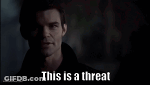A Man In A Dark Room With The Words This Is A Threat Below Him GIF