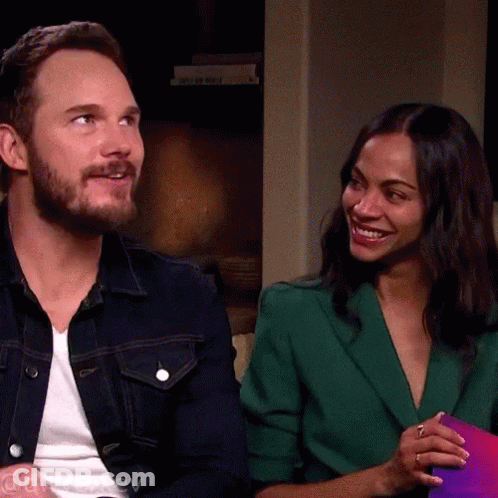 A Man In A Denim Jacket And A Woman In A Green Jacket Are Sitting Next To Each Other GIF