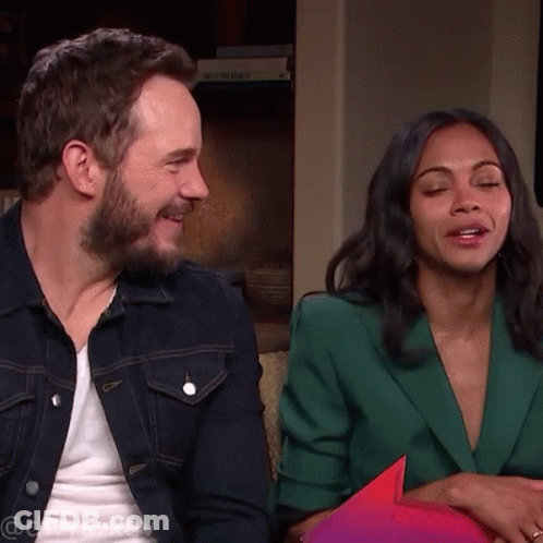 A Man In A Denim Jacket And A Woman In A Green Jacket Sit On A Couch With Their Eyes Closed GIF