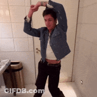 A Man In A Denim Jacket Is Dancing In A Bathroom Next To A Trash Can GIF