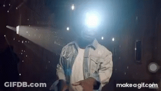 A Man In A Denim Jacket Is Dancing In Front Of A Projector Screen . GIF
