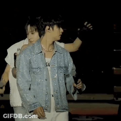 A Man In A Denim Jacket Is Holding A Microphone On A Stage GIF