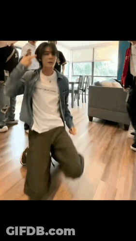 A Man In A Denim Jacket Is Kneeling Down And Dancing In A Room . GIF