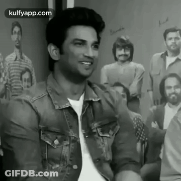 A Man In A Denim Jacket Is Sitting In Front Of A Group Of People . GIF