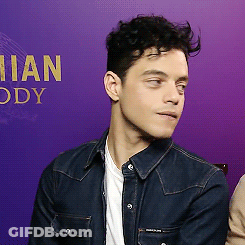 A Man In A Denim Jacket Is Sitting In Front Of A Purple Wall With The Word Ody In Gold Letters GIF