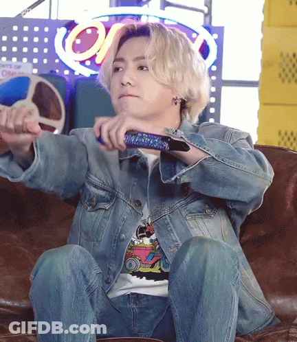 A Man In A Denim Jacket Is Sitting On A Couch Holding A Remote Control GIF