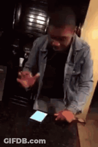 A Man In A Denim Jacket Is Standing In Front Of A Phone . GIF
