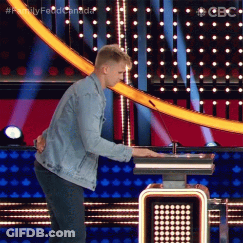A Man In A Denim Jacket Is Standing In Front Of A Podium With The Words Family Feud Canada Written On It GIF