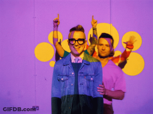 A Man In A Denim Jacket Is Standing In Front Of A Purple Background GIF