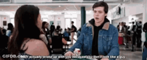 A Man In A Denim Jacket Is Talking To A Woman In A Crowded Room . GIF