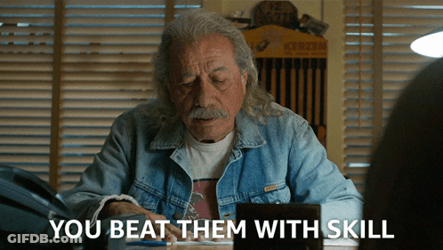 A Man In A Denim Jacket Sits At A Desk With The Words " You Beat Them With Skill " Above Him GIF