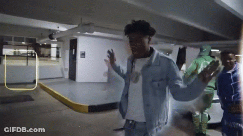 A Man In A Denim Jacket Stands In A Parking Garage With His Arms Outstretched GIF