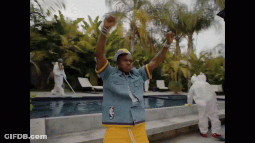 A Man In A Denim Shirt And Yellow Shorts Is Dancing In Front Of A Swimming Pool GIF