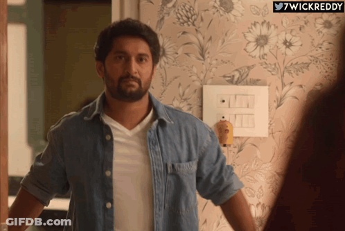 A Man In A Denim Shirt Is Standing In Front Of A Wall With Flowers On It And The Words 7Wickreddy Below Him GIF