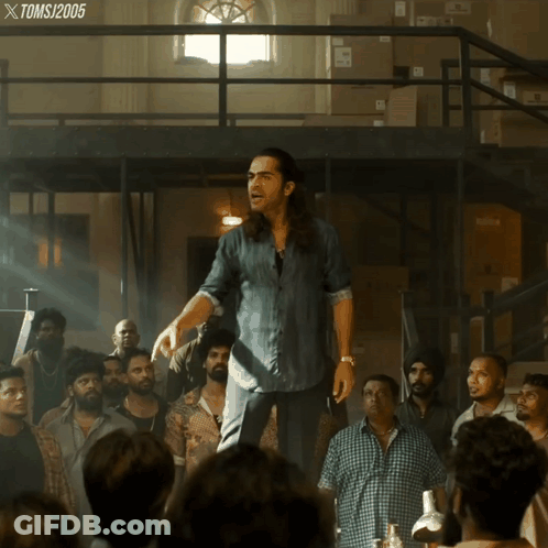 A Man In A Denim Shirt Stands In Front Of A Crowd Of People With A Toms 2005 Watermark GIF