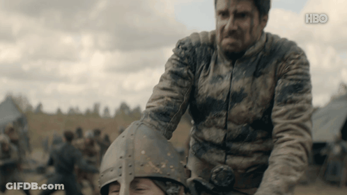 A Man In A Dirty Jacket Is Holding Another Man 'S Helmet With The Hbo Logo On The Bottom GIF