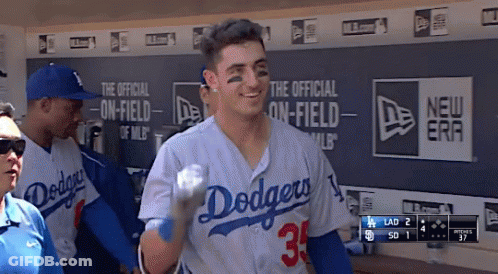 A Man In A Dodgers Jersey Holds A Baseball In A Dugout GIF