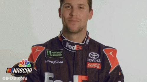 A Man In A Fedex Racing Suit Is Standing In Front Of A Nascar Logo . GIF
