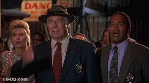 A Man In A Fedora Stands In Front Of A Sign That Says Danger GIF