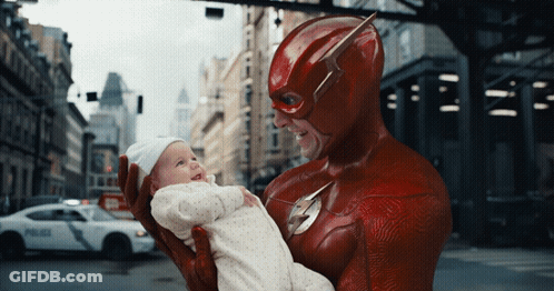 A Man In A Flash Costume Is Holding A Baby In His Arms GIF