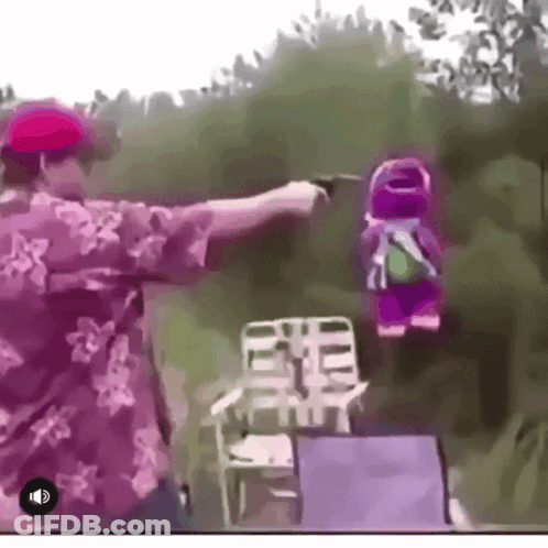 A Man In A Floral Shirt Is Pointing A Gun At A Stuffed Animal GIF