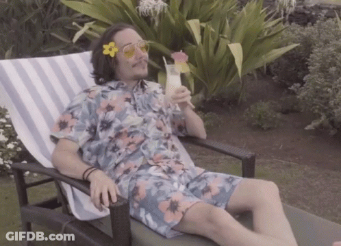 A Man In A Floral Shirt Is Sitting In A Chair Drinking A Cocktail GIF