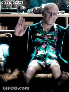 A Man In A Floral Shirt Is Sitting On A Couch And Waving His Hand GIF