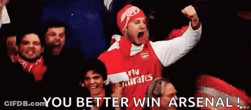 A Man In A Fly Emirates Jersey Is Holding His Fist In The Air While Sitting In A Crowd Of People . GIF