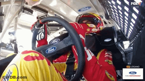 A Man In A Ford Racing Suit Is Sitting In The Driver 'S Seat Of A Race Car GIF