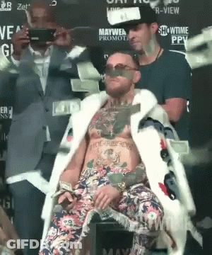 A Man In A Fur Coat Is Sitting In Front Of A Sign That Says Ppv GIF