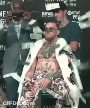 A Man In A Fur Coat Is Sitting In Front Of A Sign That Says Showtime Ppv GIF