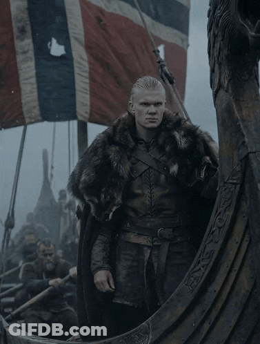 A Man In A Fur Coat Is Standing On A Viking Ship GIF