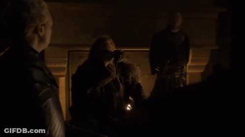 A Man In A Fur Coat Stands In A Dark Room With Two Other People GIF
