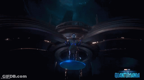A Man In A Futuristic Suit Is Standing In A Dark Room With A Blue Circle Around Him . GIF