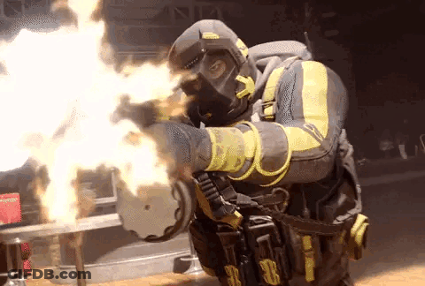 A Man In A Gas Mask Is Holding A Gun With Flames Coming Out Of It 'S Barrel . GIF