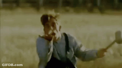 A Man In A Gas Mask Is Holding A Hammer In A Field And Making A Funny Face . GIF