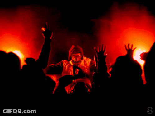 A Man In A Gas Mask Is Singing Into A Microphone In Front Of A Crowd Of People GIF