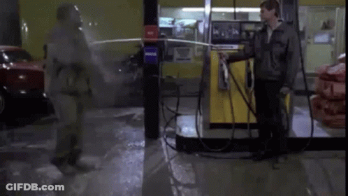 A Man In A Gas Mask Is Spraying Another Man With A Hose . GIF