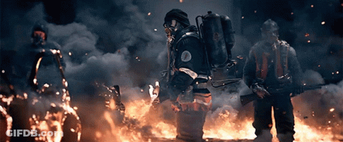 A Man In A Gas Mask Stands In Front Of A Large Fire GIF