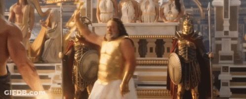 A Man In A Gold Armor Is Standing In Front Of A Statue Of A Greek God . GIF