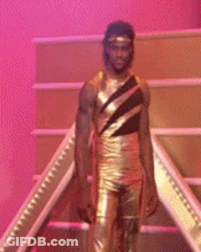 A Man In A Gold Leotard Is Standing On A Set Of Stairs GIF