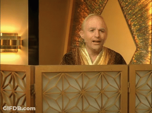 A Man In A Gold Robe Stands In Front Of A Wooden Screen GIF