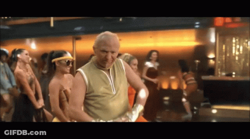 A Man In A Gold Tank Top Is Dancing In Front Of A Crowd Of Women GIF