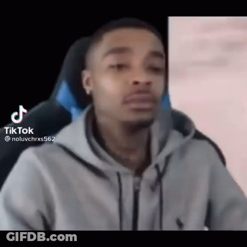 A Man In A Gray Hoodie Is Sitting In A Chair And Making A Funny Face . GIF
